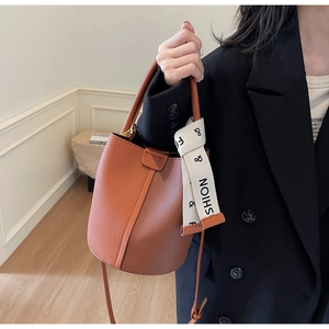 Detail of dark brown lychee leather bucket bag with fashion printed ribbon and metal logo