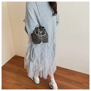 Vue détaillée d'un sac seau en tweed noir avec chaînes et perles porté par un modèle