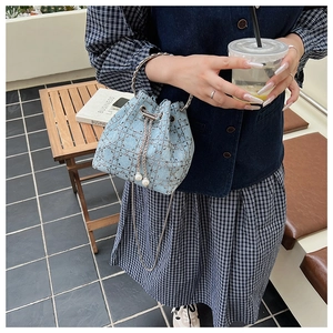 Détail du sac seau en jean bleu clair avec clous argentés et bandoulière chaîne au café