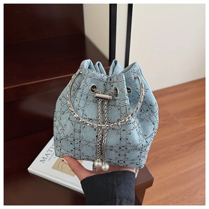 Détail d'un sac seau en denim avec clous en métal argenté et cordon en perles