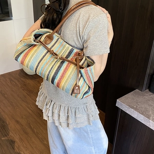 Colorful striped woven tote bag with brown leather handles shown on a model