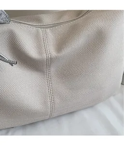 Detail shot of the beige herringbone fabric texture and silver zipper on the tote bag