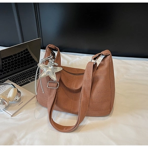 Brown knitted tote bag with silver star charm and wide shoulder strap on white desk