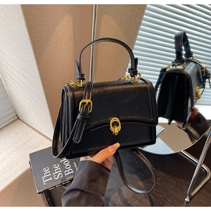 Detail of glossy black leather handbag with gold double ring buckle on wooden surface