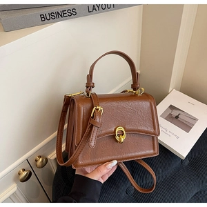 Detail view of vintage brown leather handbag with gold oval twist lock and retro texture