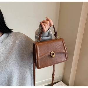 Brown textured leather crossbody bag detail with golden rings and top handle worn by model