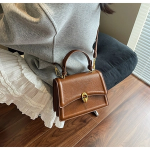 Detail of vintage brown textured PU leather bag with gold double-ring clasp on a model