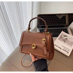 Close-up of brown textured leather bag with gold clasp on office desk setup
