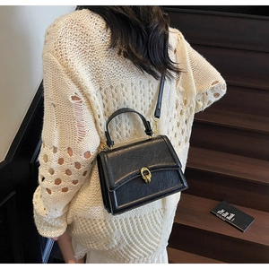 Macro detail of a black textured faux leather crossbody bag with gold metallic buckle