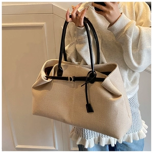 Detail of canvas tote bag showing beige textured fabric and black leather strap details