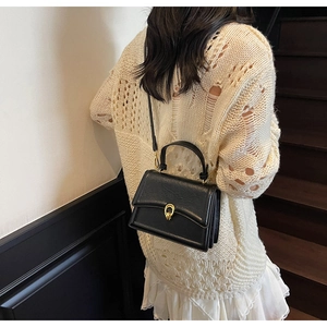 Detail of a black crossbody bag with gold horseshoe clasp and textured finish