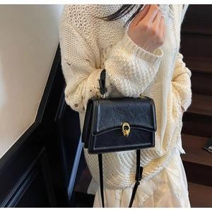 Detail of vintage black textured crossbody bag with gold ring lock on white sweater