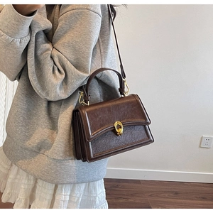Deep brown textured leather crossbody bag with a gold oval lock shown on a model