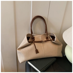 Detail of a large beige woven tote bag with premium brown leather straps and gold buckle