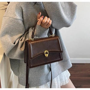 Brown retro crossbody bag with golden twist lock worn with a casual fashion outfit