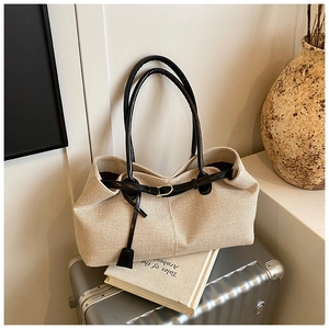 Close-up of beige woven canvas tote bag with black leather straps on a silver suitcase