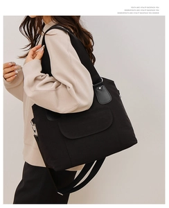 Vue détaillée du sac cabas noir en toile montrant les poignées et la bandoulière large