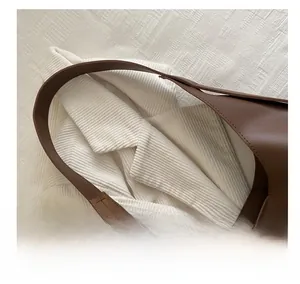 Close-up of brown leather tote bag strap and matte texture on white corduroy