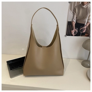 Detailed side view of a large khaki hobo bag on a desk with a laptop and lamp