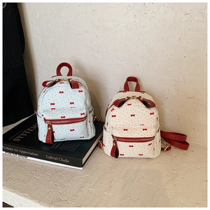 Detail of mini backpacks with red bow prints and contrasting red straps on white surface