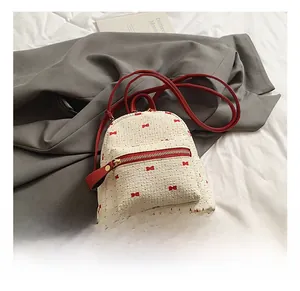 Detail of white knit mini backpack with red bow embroidery and slim red leather straps
