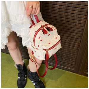 Detail of cream woven backpack featuring red ribbon patterns and gold hardware