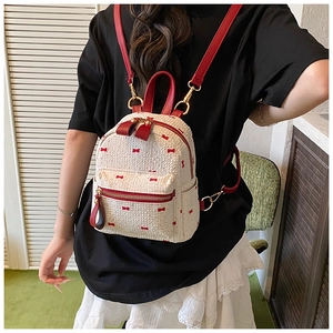 Close-up of a mini backpack featuring textured cream fabric and red bow patterns on a model