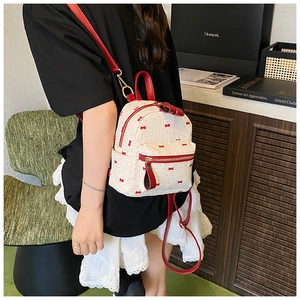 Detail of a mini woven backpack featuring red bow patterns and leather straps on a model