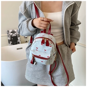 Close-up of light blue woven backpack with red bow pattern and red leather straps