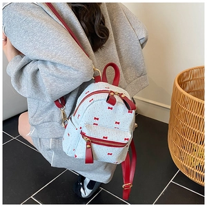 Close-up of white mini backpack with red bow patterns and adjustable red straps