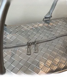Detail of silver woven handbag showing smooth metallic dual zipper and texture