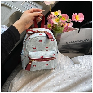 Detailed view of mini blue backpack with red bow prints and leather handle in a car