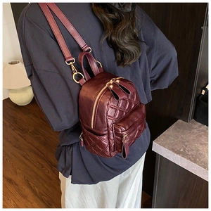 Detail view of burgundy quilted mini backpack with gold hardware and side pocket features
