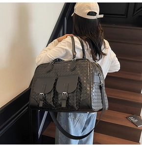 Model wearing large black woven tote bag with adjustable shoulder strap and metal buckles