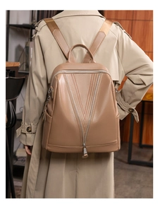 Detail of khaki pebbled leather backpack showing V-shaped stitching and woven shoulder strap