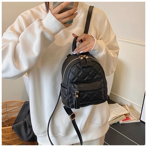 Detailed view of black quilted mini backpack with gold zippers shown on a model
