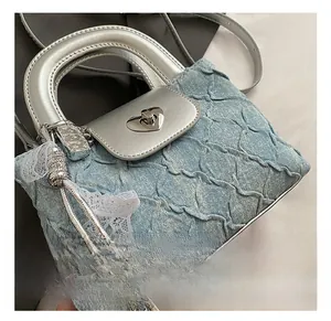 Close-up of heart-shaped metal twist lock on light blue denim bucket bag with lace bow