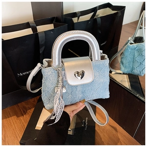 Detail of light blue denim mini bag with silver heart lock and white lace charm