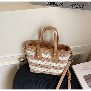 Detail of woven straw bucket bag with brown leather handles and golden metal rivets