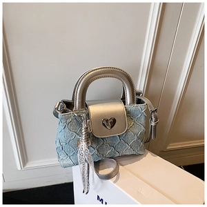 Macro detail of quilted denim handbag with silver heart lock and lace tassel charm