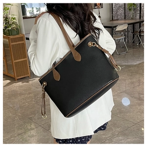 Detail of a large black leather tote bag with brown straps and side tassel on model