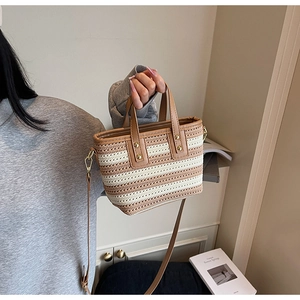 Detail of woven bucket bag with brown leather handle and gold hardware on beige stripes