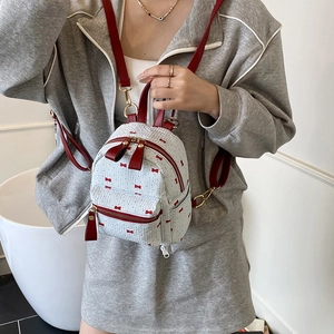 Mini white backpack with red bow prints and leather straps worn by a model