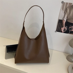 Minimalist large brown leather hobo bag for women with wide shoulder strap on a white desk