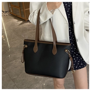 Detailed view of black and brown tote bag with gold metal rings on shoulder