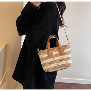Detail of woven straw bucket bag featuring brown faux leather trim and metallic rivets
