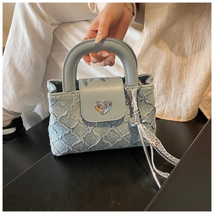 Detail of light blue denim handbag featuring a silver heart-shaped twist lock and lace tassel
