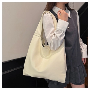 Close-up of a large cream leather tote bag shown on the shoulder of a model in a minimal room