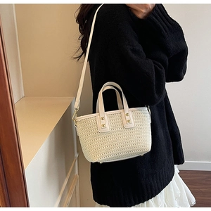 Detail of cream hand-woven bucket bag with white leather handle and golden metal rivets