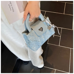 Detail of light blue denim handbag featuring a heart-shaped metal twist lock and texture